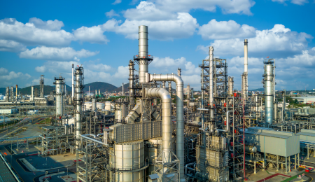 An oil refinery in the foreground, and mountains, blue sky and clouds in the background.