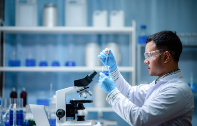 A male scientist putting chemicals into a beaker using a pipette.