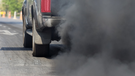A black truck driving on a road with black smoke coming from the tail pipe.