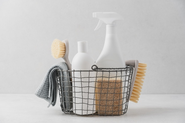 a basket holding various cleaning supplies: sponges, scrubbers, a towel, and a spray bottle 